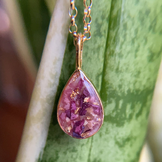 Teardrop-shaped purple pendant on a chain against a green leafy background